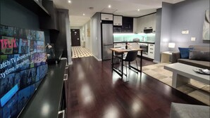 A modern living room with a flat-screen TV, a dining area, a kitchen, and a hallway leading to a door. - Chic and Renovated 1bd/1bth (Cape Town)