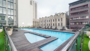 A rooftop pool with a wooden deck, surrounded by modern buildings with balconies and a glass facade. - Chic and Renovated 1bd/1bth (Cape Town)