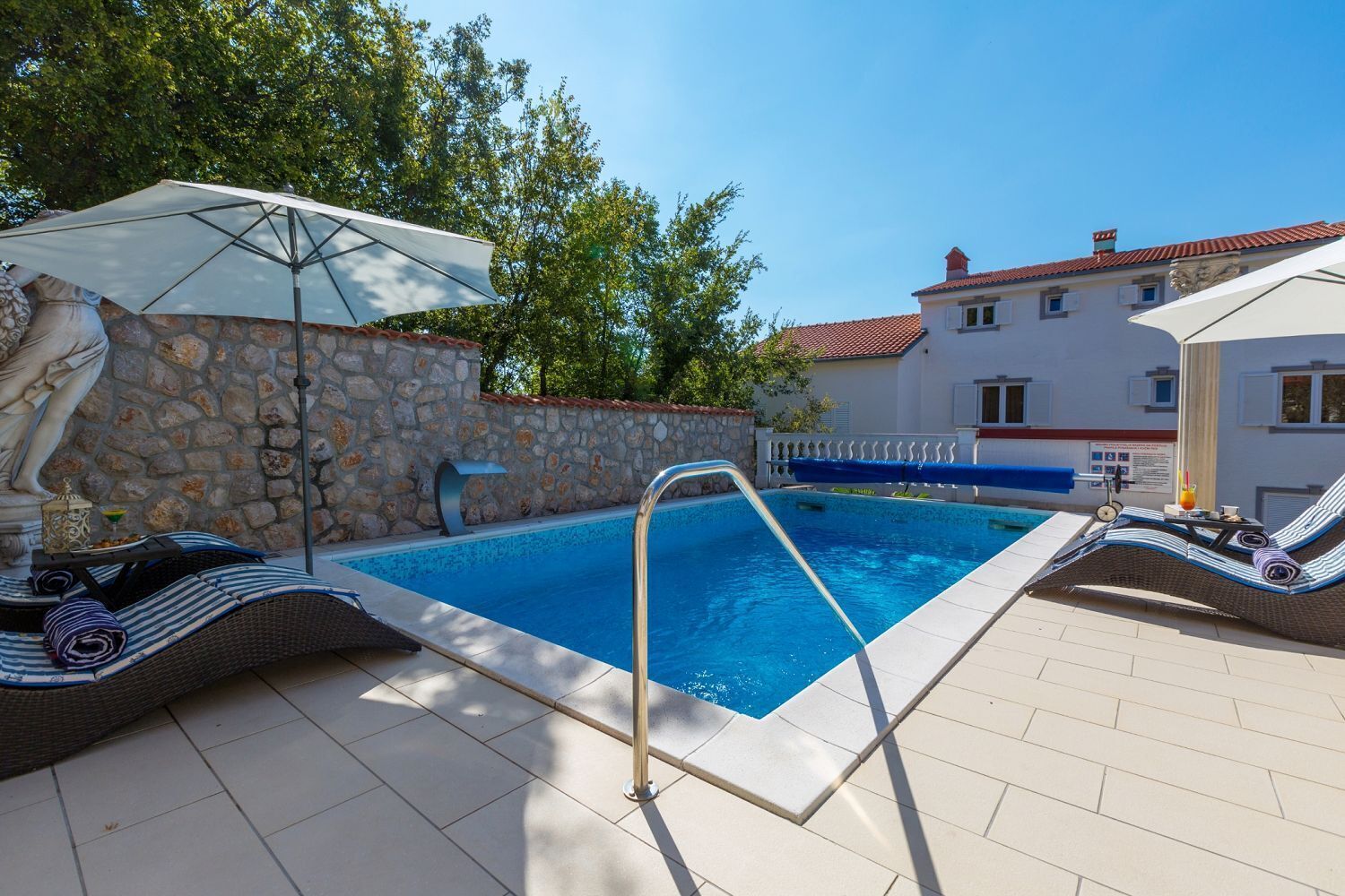 Una piscina amb una paret de pedra i un edifici blanc al fons.
