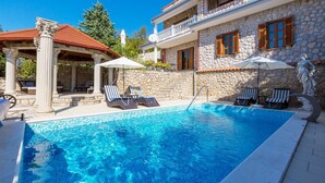 A swimming pool with lounge chairs and umbrellas, stone walls, and a covered area with columns. - Charming flat just 700 metres from the beach with sea views, pool, BBQ, private parking (Crikvenica)