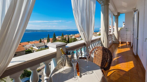 A balcony with a table set for dining, overlooking a coastal town and the sea. - Unique flat with magnificent sea views, pool, BBQ and only 700 metres to the beach (Crikvenica)