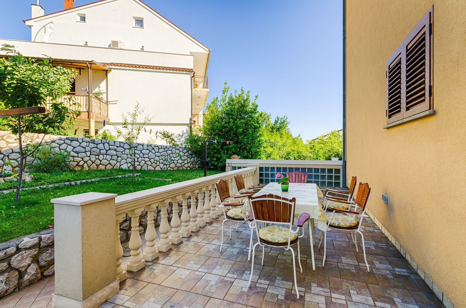 A patio with a table and chairs, a stone wall, and a building in the background.