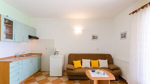 Un espace de vie compact comprenant un coin cuisine, un canapé marron avec des coussins jaunes, une petite table avec un bol et un verre bleus, et un radiateur blanc.