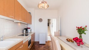 Una cocina moderna con armarios de madera, horno empotrado, microondas y cafetera. Hay un comedor con una mesa preparada para dos, un jarrón con flores rojas y un plato de manzanas.