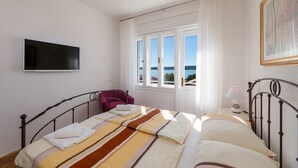 Un dormitorio con cama, una silla, televisión, ventana con vistas y una lámpara.