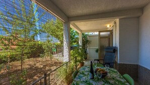 Eine überdachte Terrasse mit Tisch für zwei Personen, einem Stuhl und einem Blumentopf.