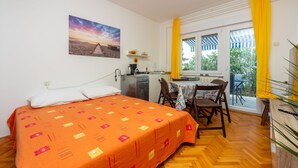 A room with a bed, a small kitchenette, a dining table with chairs, and a window with yellow curtains. - Fantastic flat only 150 metres to the beach with sea view, sun lounger, barbecue, dog-friendly (Dramalj)