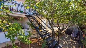 A residential building with a staircase leading to a balcony, surrounded by trees and outdoor furniture. - Fantastic flat only 150 metres to the beach with sea view, sun lounger, barbecue, dog-friendly (Dramalj)