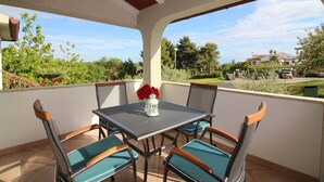 Une terrasse couverte avec une table et des chaises, une vue sur la verdure et les maisons environnantes, et un ciel dégagé.