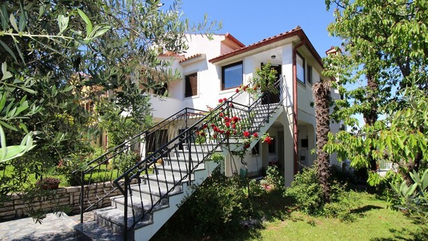 Une maison à deux étages avec un escalier en pierre menant à un balcon orné de fleurs rouges.
