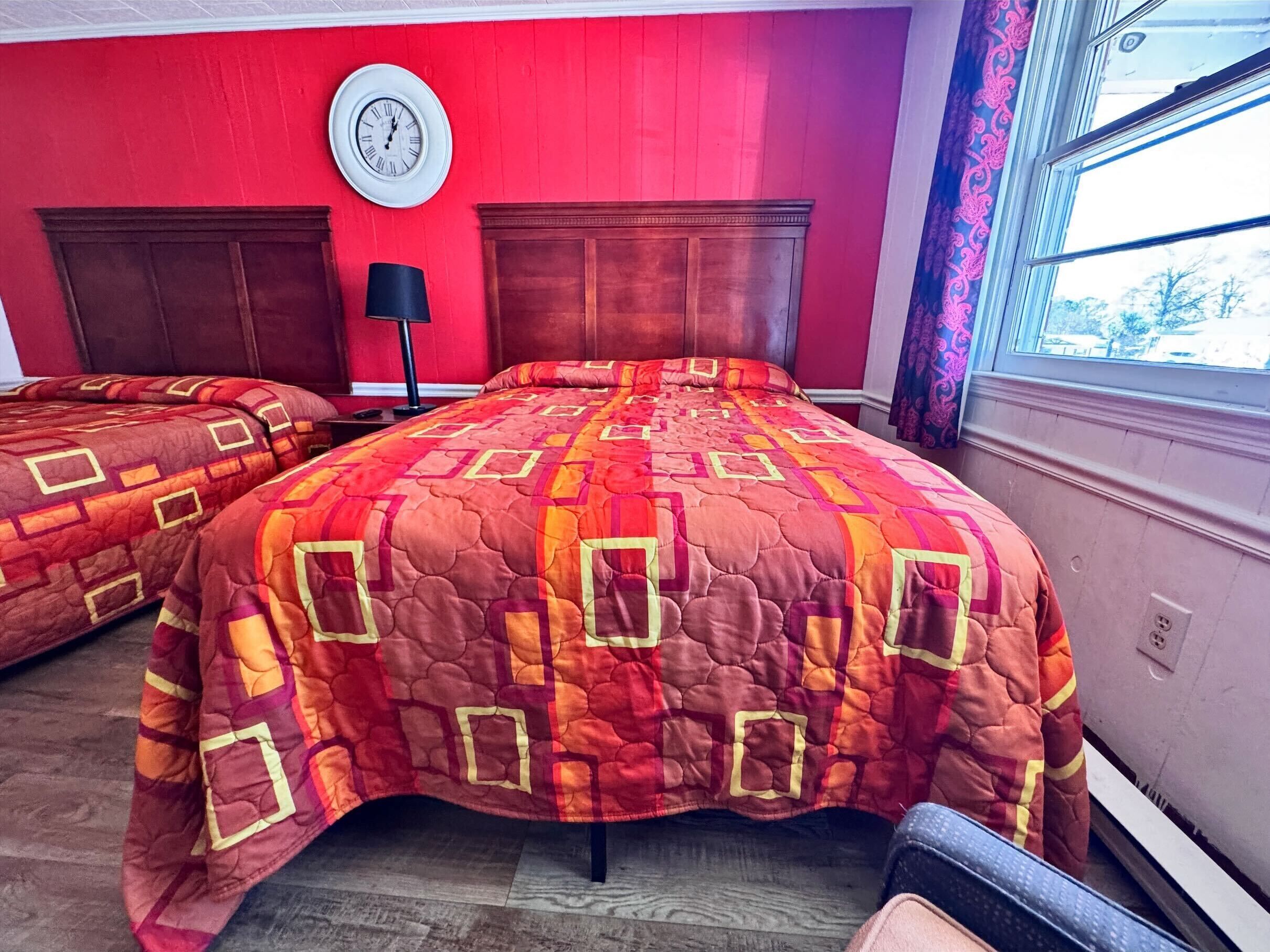 Un dormitorio con dos camas, un reloj en la pared y una ventana con cortinas.