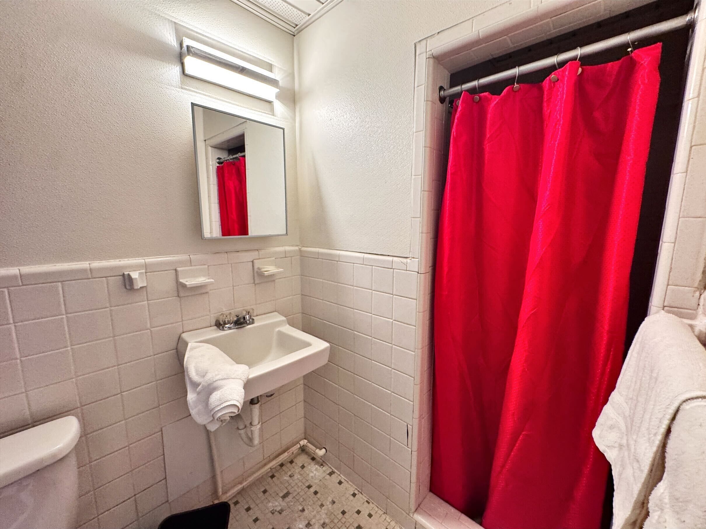 A bathroom with a white sink, a mirror, and a red shower curtain.