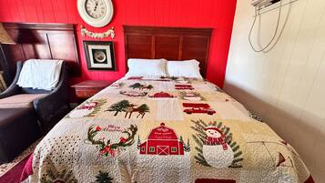 Habitación de hotel con pared roja, cabecera de madera, cama con colcha navideña, un reloj y un cuadro enmarcado.