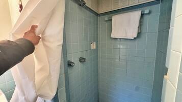 Un baño con paredes de azulejos azules, una toalla blanca colgada en un perchero y una cortina de ducha que se está acomodando.