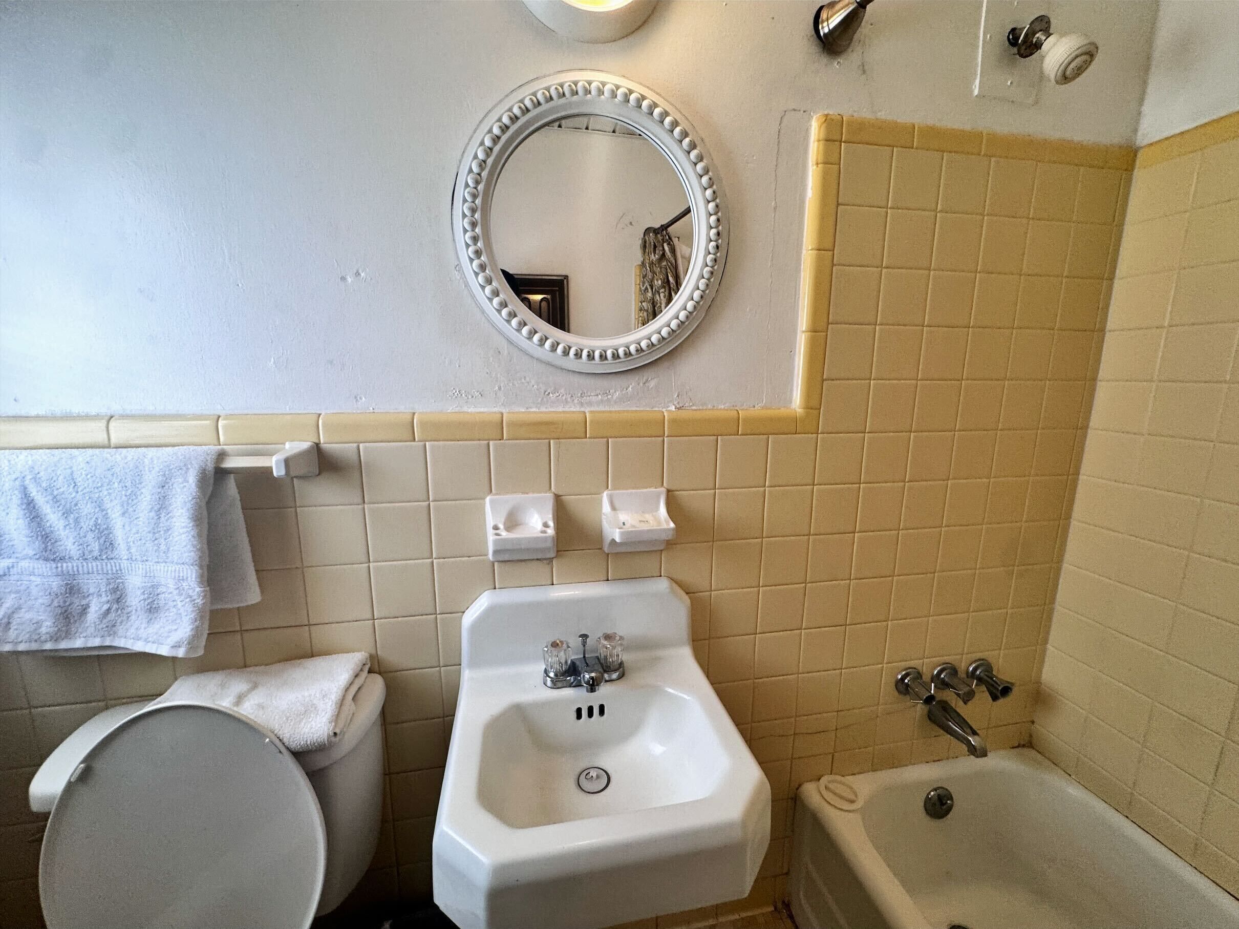 Un baño con inodoro, lavamanos y bañera. Hay un espejo sobre el lavamanos y un perchero en la pared.