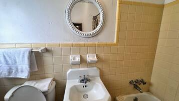 Un baño con inodoro, lavamanos y bañera. Hay un espejo sobre el lavamanos y un perchero en la pared.