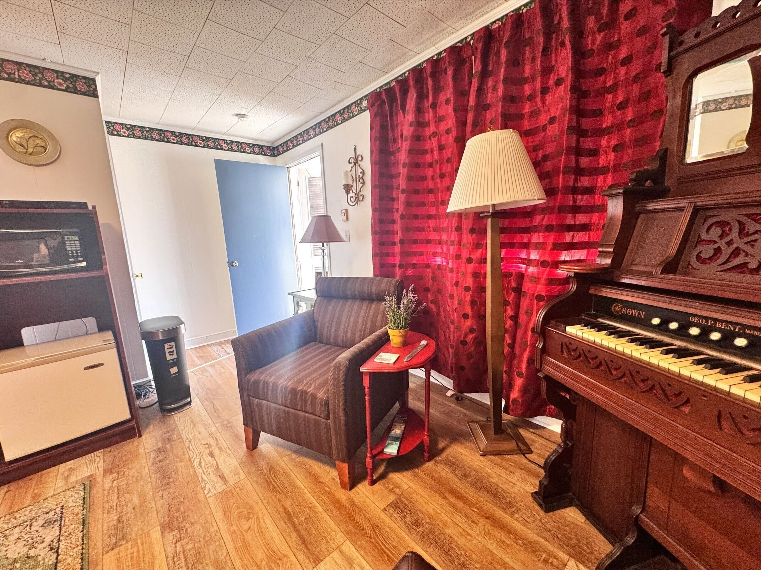 A living room with a piano, a sofa, a small table with a lamp, and a microwave.