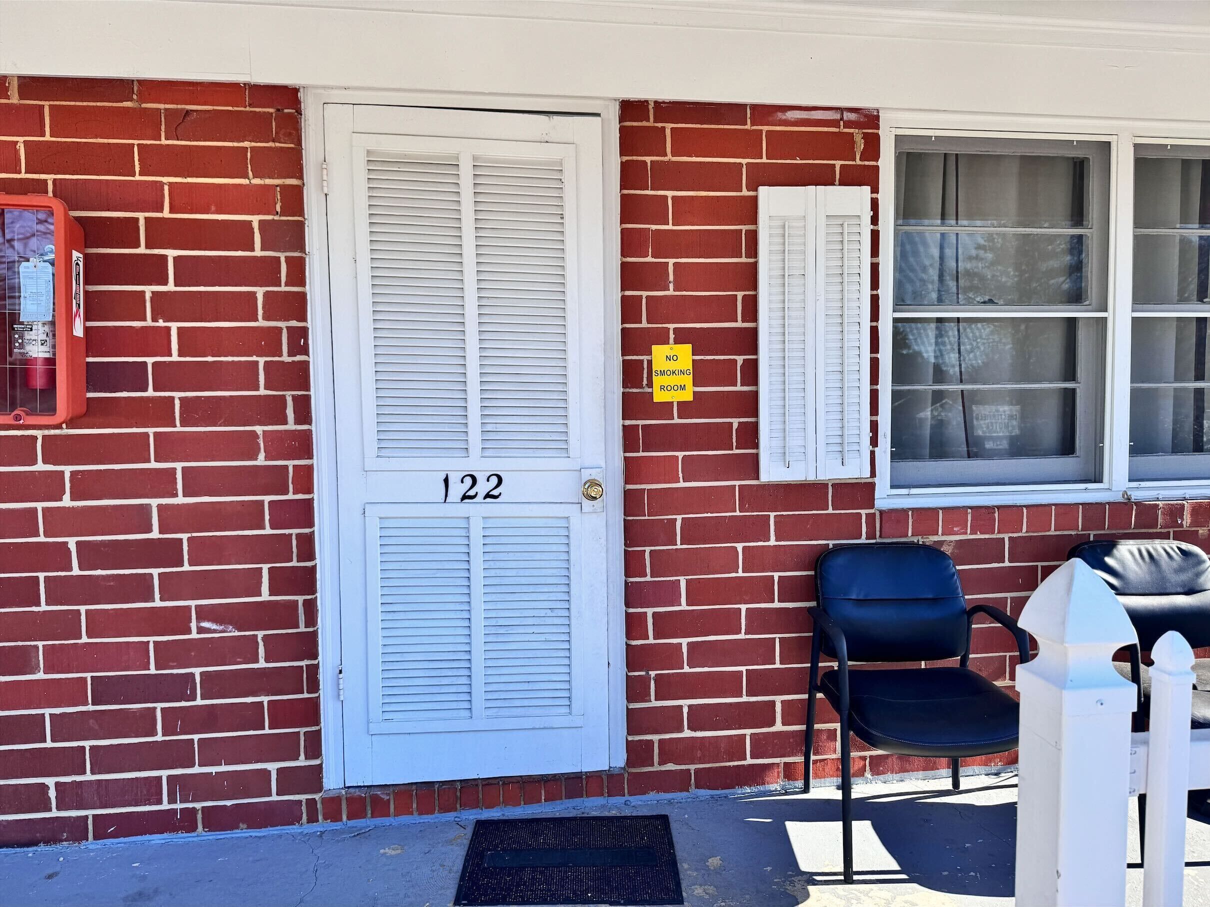A red brick building with a white door labeled "122" and a "NO SMOKING" sign.