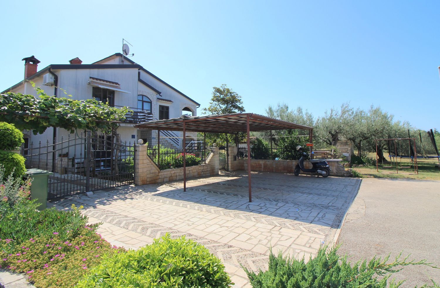 A house with a paved driveway, a covered patio, and a garden with various plants and flowers.