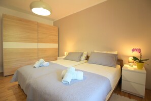 Ett modernt hotellrum med två sängar, en garderob i trä, ett nattduksbord med en lampa och en orkidé i en kruka.