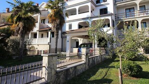A multi-story residential building with balconies, a stone wall, and a car parked in front. - Charming top floor apartment with sea view and view of the old town of Porec (Porec)