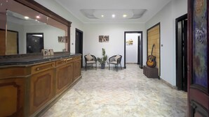 A spacious hallway with a marble floor, a wooden reception desk, two chairs, a potted plant, and a guitar leaning against the wall. - Pyramids Sunlight Hotel (Giza)