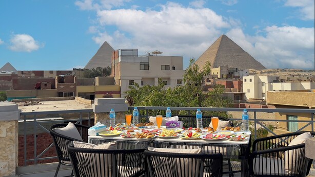 A table set with various dishes and drinks on a balcony overlooking pyramids and buildings. - Pyramids Sunlight Hotel (Giza)