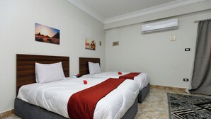 A hotel room with two beds, a marble floor, a wall-mounted air conditioner, and artwork. - Pyramids Sunlight Hotel (Giza)