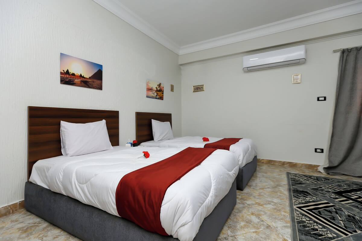 Quarto de hotel com duas camas, piso de mármore, ar condicionado fixado na parede e obras de arte.
