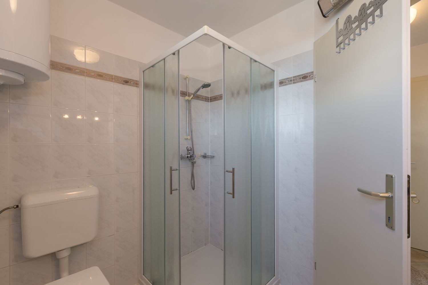 Ein modernes Badezimmer mit einer Duschkabine aus Glas, weißen Fliesen und einer Toilette.