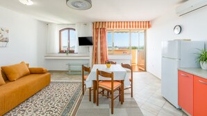 A compact living space with a sofa, dining table, chairs, a TV, and a kitchen area with a refrigerator. - Idyllic flat just 250 metres from the beach with pool, sea view, barbecue area, loungers (Porec)