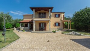 A two-story house with a balcony, a covered patio, and a paved driveway. - Fantastic flat just 250 metres from the beach with sea views, pool, barbecue area, private parking space (Porec)