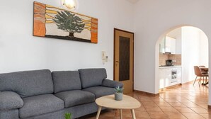 A living room with a grey sofa, a small round table with a plant, and a painting of a tree. - Fantastic flat just 250 metres from the beach with sea views, pool, barbecue area, private parking space (Porec)