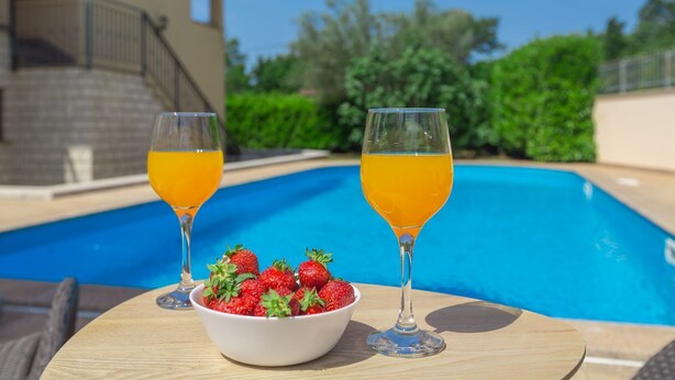 A poolside table with two glasses of orange juice and a bowl of strawberries. - Fantastic flat just 250 metres from the beach with sea views, pool, barbecue area, private parking space (Porec)