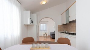 A modern kitchen with white cabinets, a stove, and a microwave. There is a dining table with chairs and a tray of glasses. - Fantastic flat just 250 metres from the beach with sea views, pool, barbecue area, private parking space (Porec)