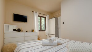 A bedroom with a bed, a TV mounted on the wall, a window with curtains, a bedside table with a mirror, and a door leading to another room. - Dog-friendly paradise with pool, playground, barbecue area, private terrace (Sveti Lovrec)