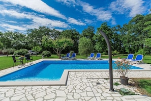 Une piscine rectangulaire bordée d’un revêtement de sol en pierres, entourée de chaises longues bleues et d’une petite table avec des chaises.