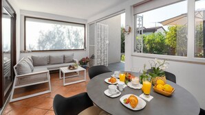 A modern dining area with a round table set for breakfast, a sofa, and a view of greenery outside. - Exquisite holiday home with private garden, sun loungers, high chair, washing machine - only 700 metres to the beach (Porec)