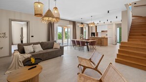 A modern living room with a sofa, dining table, wicker chairs, and a kitchen area with a staircase. - Impressive villa with panoramic views, private pool, table tennis, table football, playground, baby cot (Pazin)