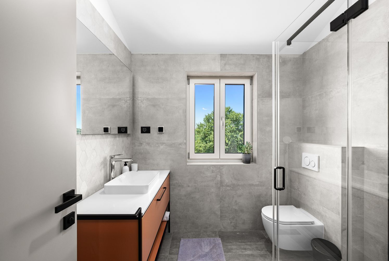 A modern bathroom with a large window, a shower, and a toilet.