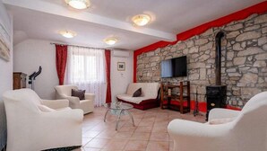 A living room with white sofas, a glass coffee table, a stone wall, a fireplace, and a TV mounted on the wall.