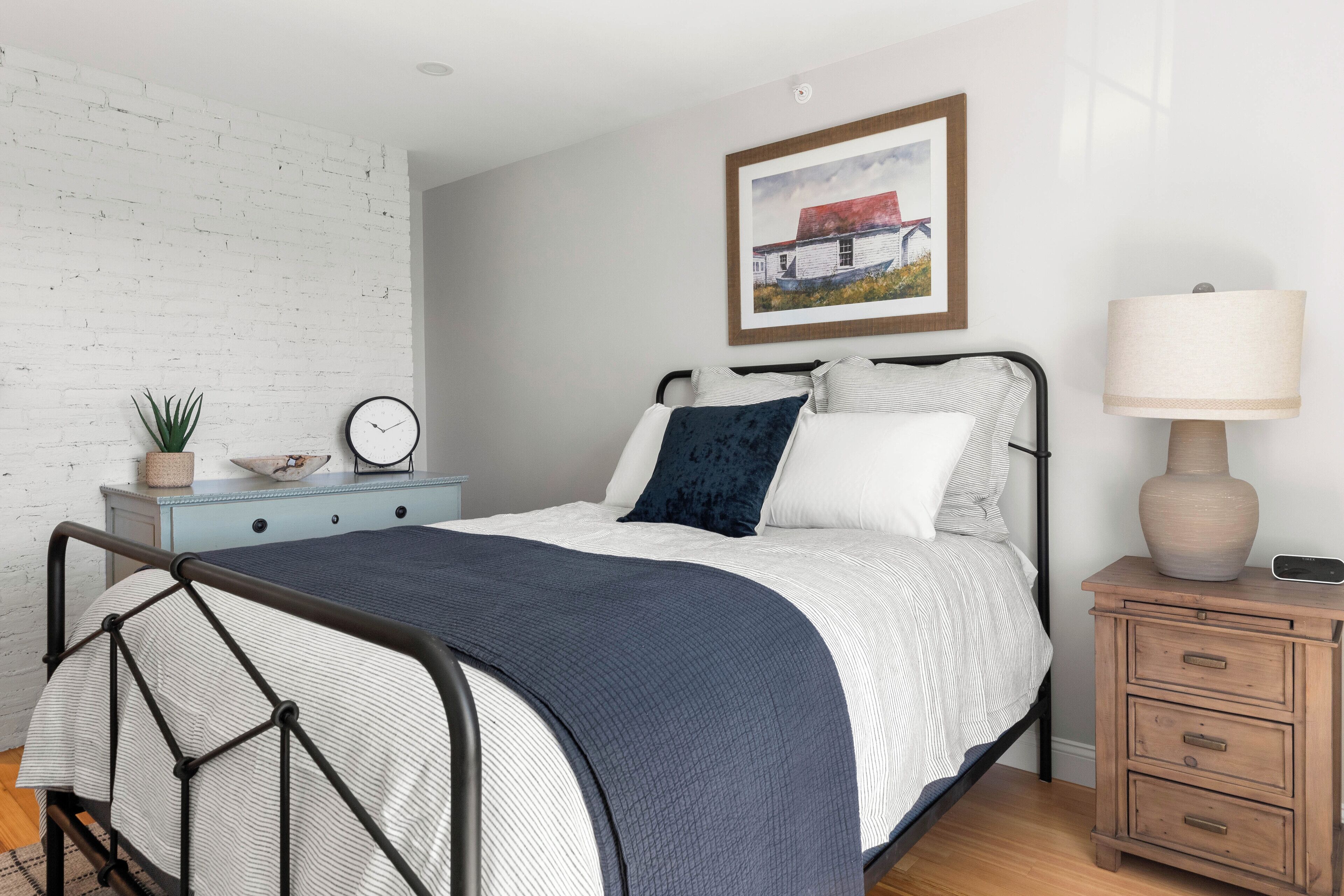 Een keurig opgemaakt slaapkamer met een bed, nachtkastje, lamp en een wandklok.