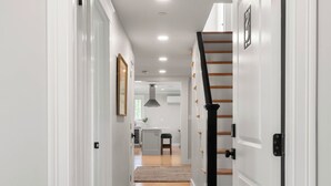 Un pasillo con suelo de madera, paredes blancas y una escalera con barandillas negras.