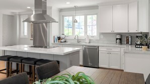 Una cocina moderna con armarios blancos, electrodomésticos de acero inoxidable y una isla central con taburetes de bar.