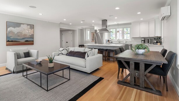 Una sala de estar moderna con un sofá blanco, una mesa de centro y una zona de comedor con una mesa y sillas de madera.