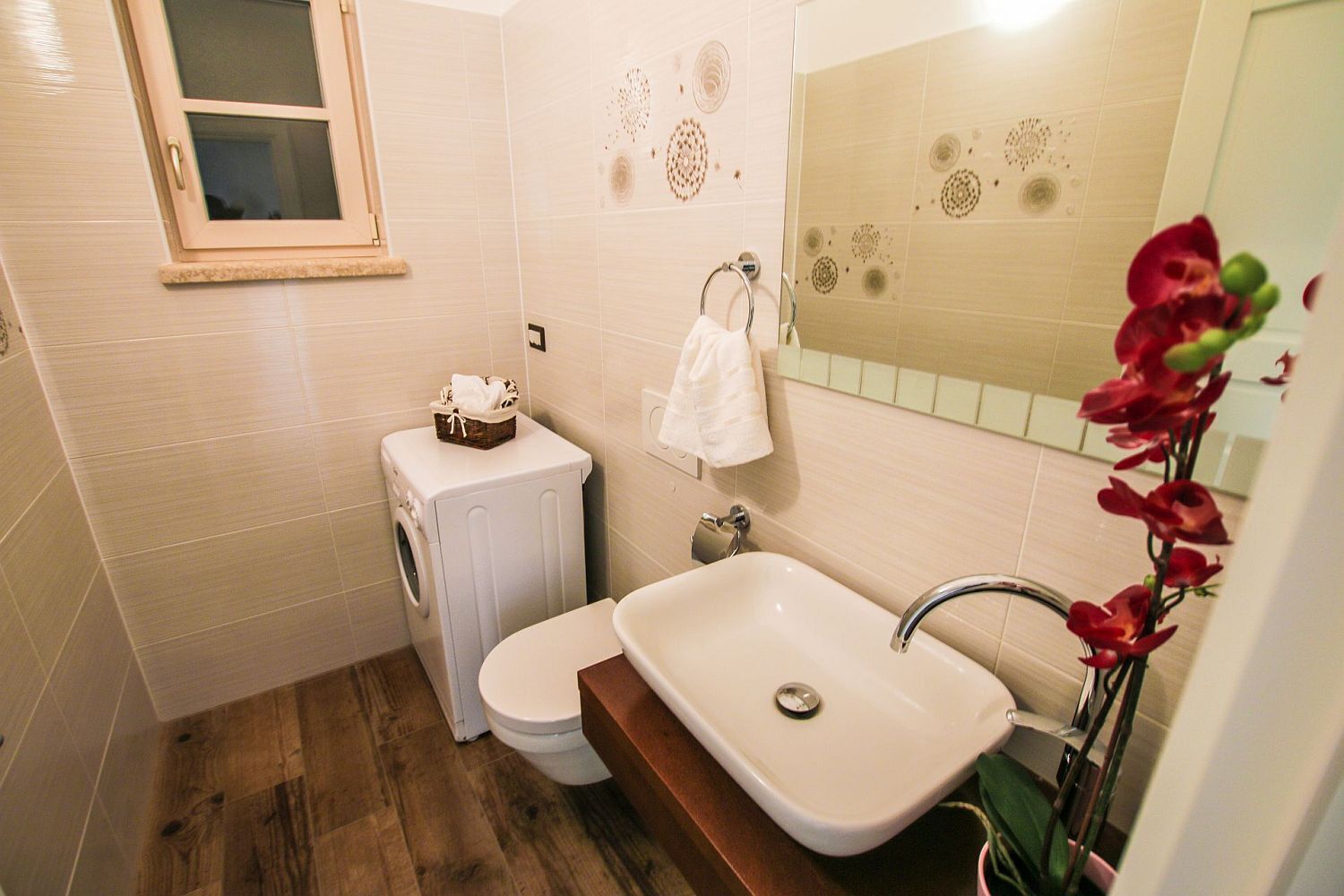 A compact bathroom with a washing machine, toilet, sink, and decorative tiles.