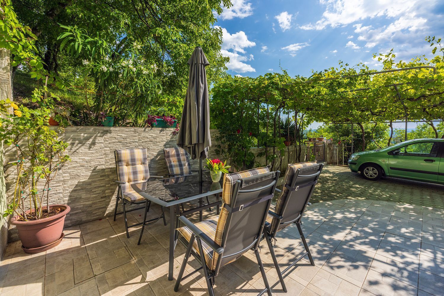 Eine Terrasse im Freien mit Tisch, Stühlen, einem Blumentopf und einer Steinmauer.