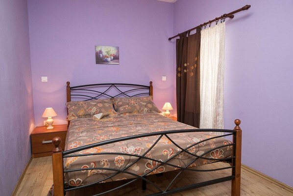 Une chambre à coucher avec un lit, deux tables de chevet avec des lampes, une fenêtre avec des rideaux et un petit tableau accroché au mur.