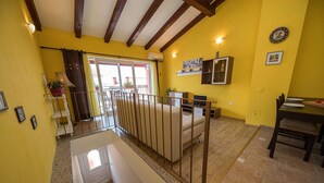 Una habitación luminosa de color amarillo con techo de madera, un sofá, una mesa de comedor y una escalera.