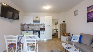 A modern living room with a sofa, a dining area with chairs and a table, a kitchen with cabinets and a stove, and a TV mounted on the wall. - Renovated flat with sea view, fitness room, baby cot, barbecue area (Crikvenica)